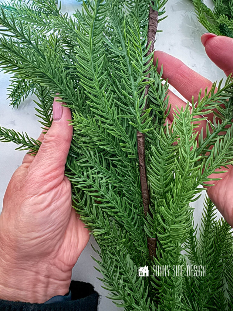 Woman holds pine faux garland.