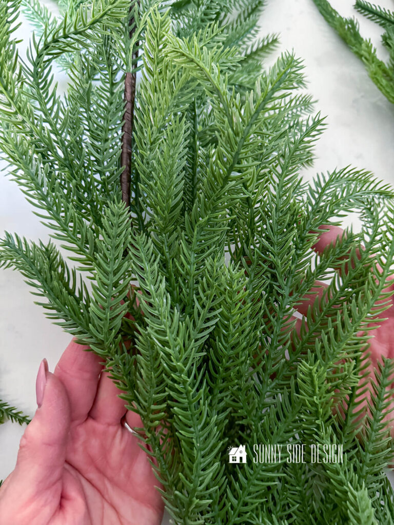 Woman holds pine faux garland.