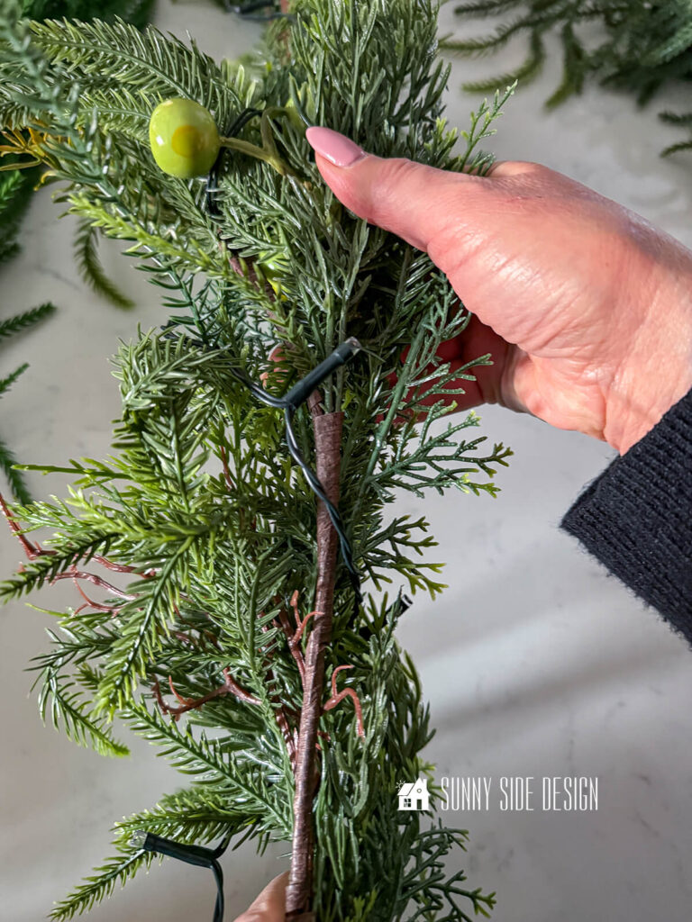Woman holds garland showing the back side of pine garland with green apples.