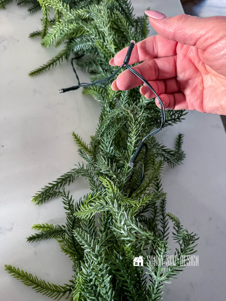 Woman holds light strand on a pine garland.