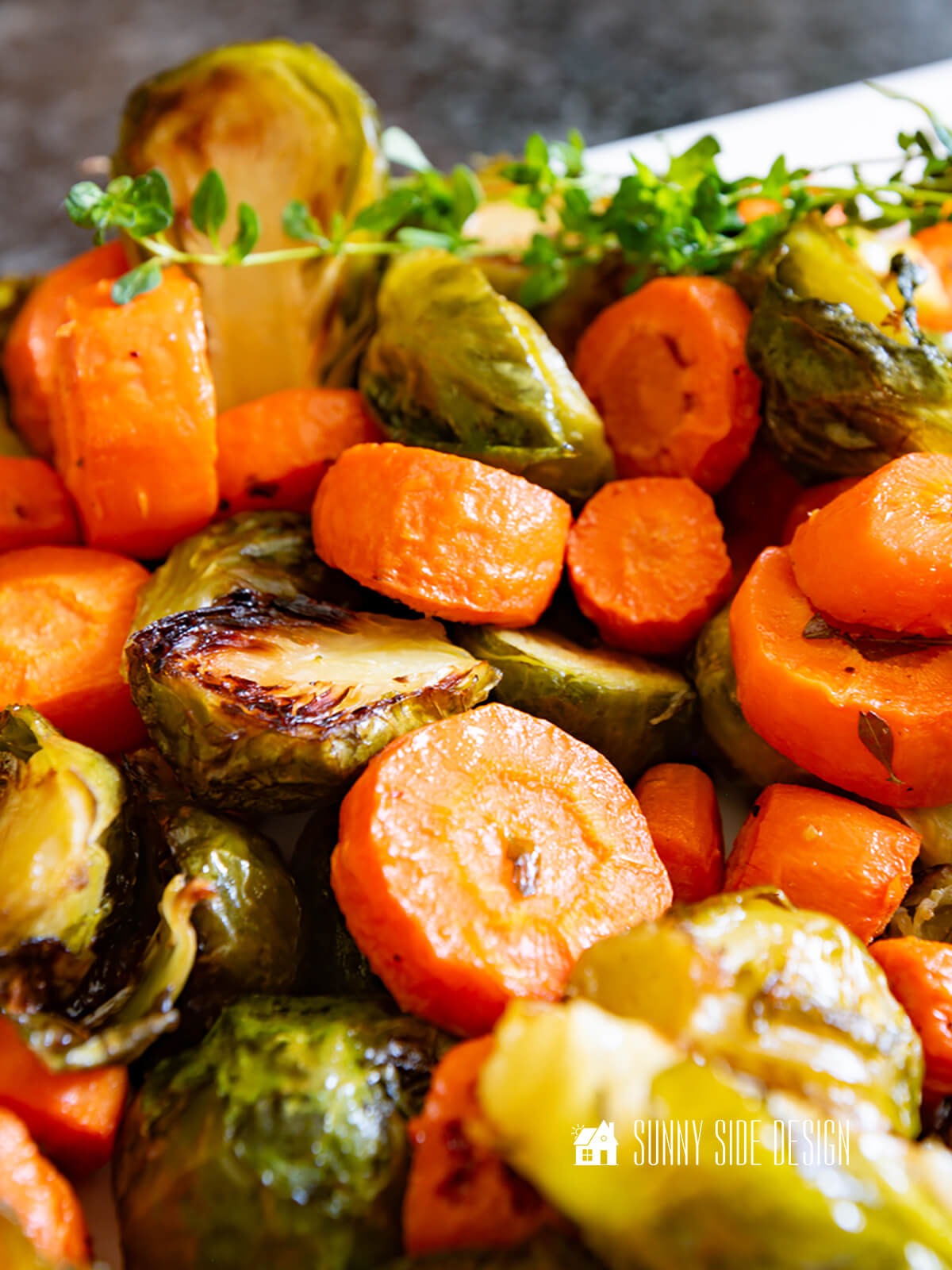 Crispy, browned roasted carrots and brussel sprouts, garnished with fresh thyme on a platter.