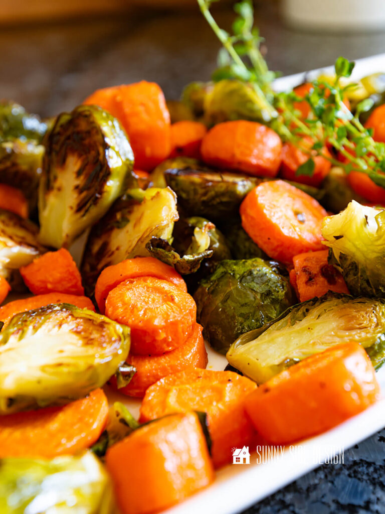 Crispy, browned roasted carrots and brussel sprouts, garnished with fresh thyme on a platter.