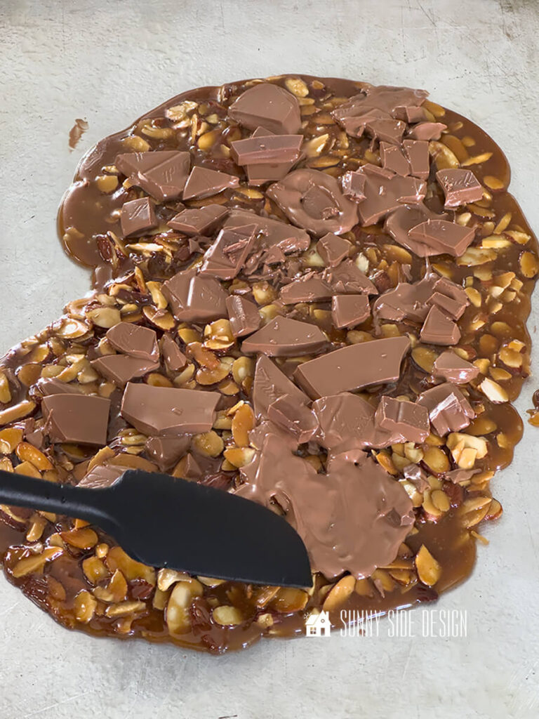 Spatula spreads melted chocolate on the hot toffee layer.