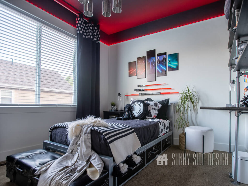 Stephanie's home tour - Star Wars themed bedroom with a black ceiling, painted wall mould to conceal LED lights, white walls, black curtains with stenciled circles, black Star Wars bedding, light sabers hung over the bed with 5 Star Wars art pieces.
