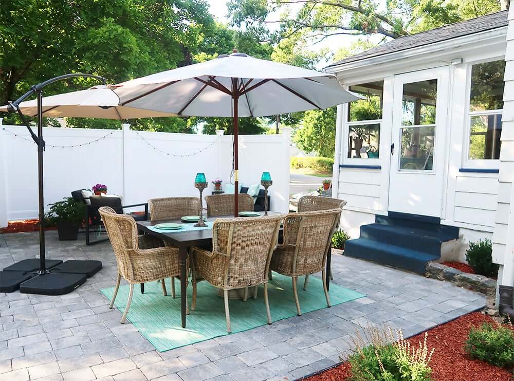 DIY grey paver patio styled with a turquiose rug and and outdoor dining set with umbrella.