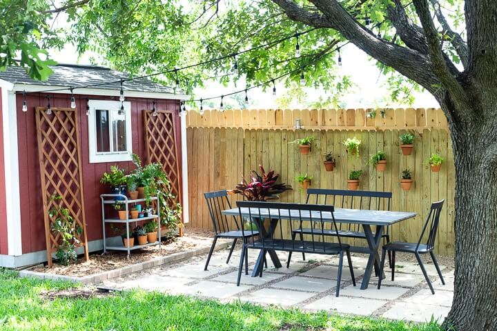 DIY pea gravel and concrete paver patio styled with an outdoor dining set and a red shed.