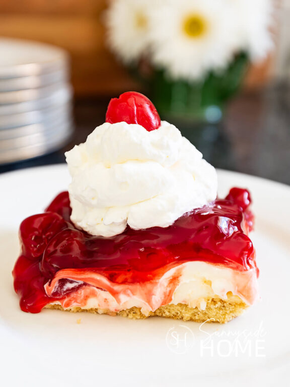 Slice of grandma's best cherry cheesecake recipe garnished with whipped cram and a maraschino cherry.