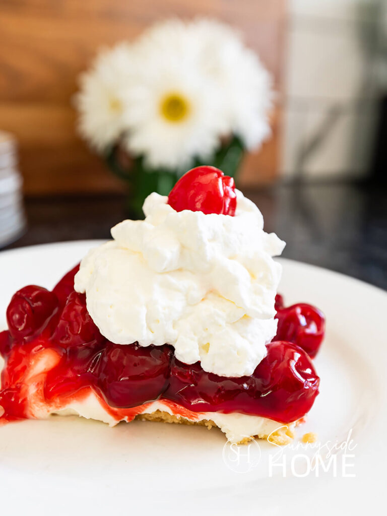 Slice of grandma's best cherry cheesecake recipe garnished with whipped cram and a maraschino cherry.