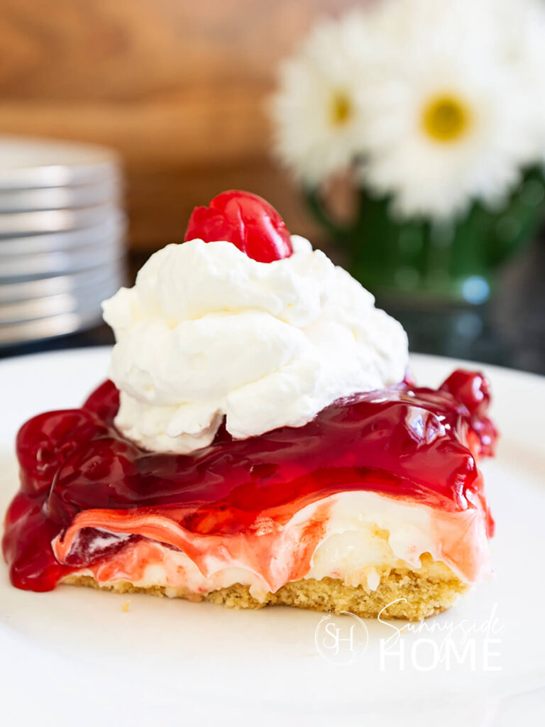 Slice of grandma's best cherry cheesecake recipe garnished with whipped cram and a maraschino cherry