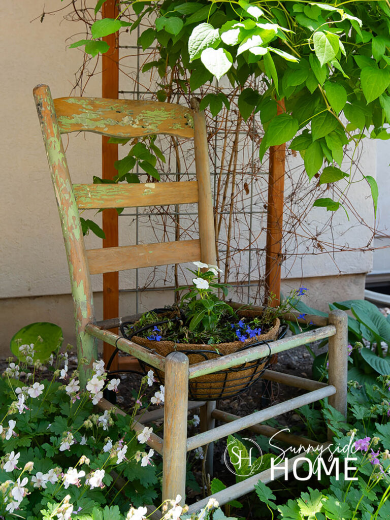 DIY chair planter nestled in the garden amount the flowers.
