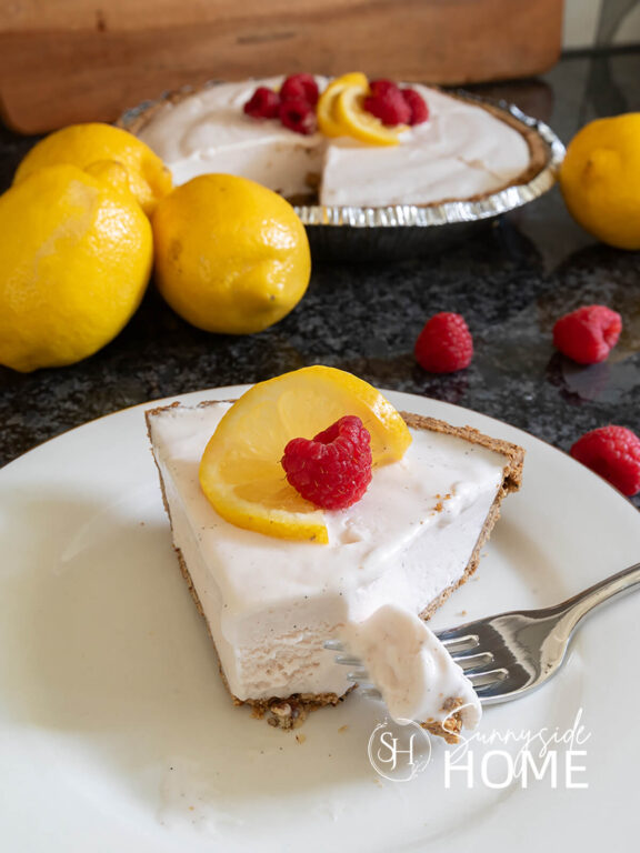 Cool and refreshing lemonade pie recipe, slice of pie and a piece on a fork, garnished with lemon slice and raspberry.