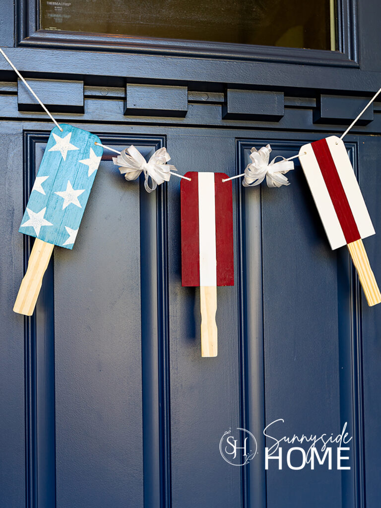 Patriotic popsicle decor bunting hung on a navy blue door. Made with paint stir sticks.