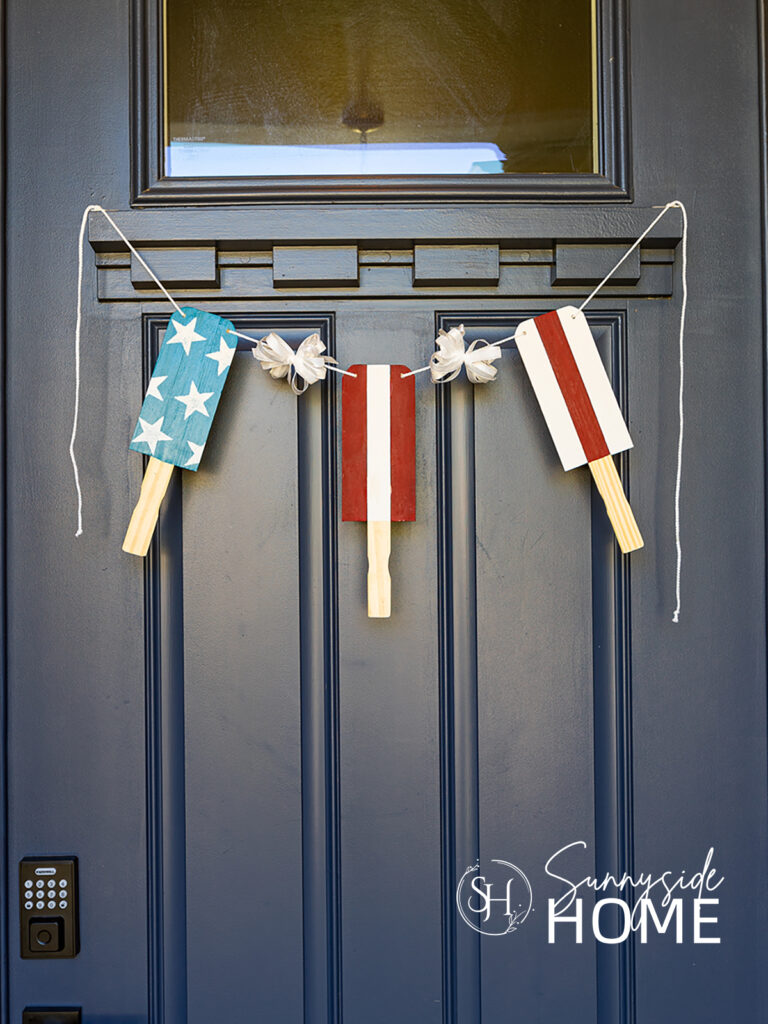 Patriotic popsicle decor bunting hung on a navy blue door. Made with paint stir sticks.