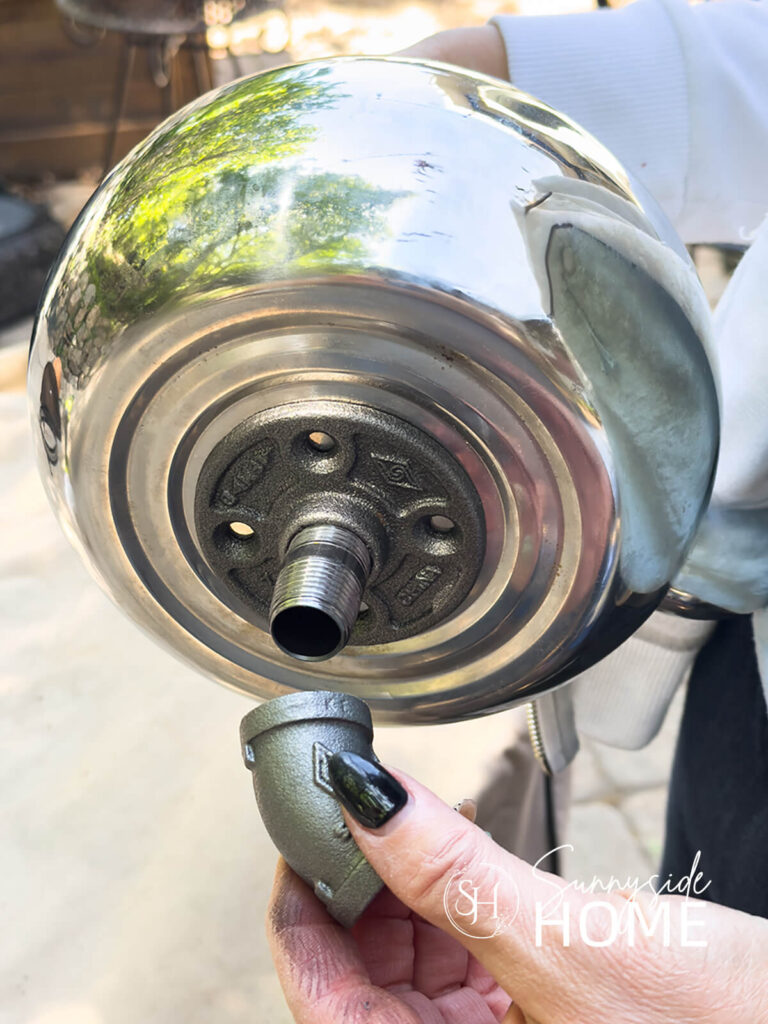 Woman threads elbow onto nipple that is attached to a teapot.