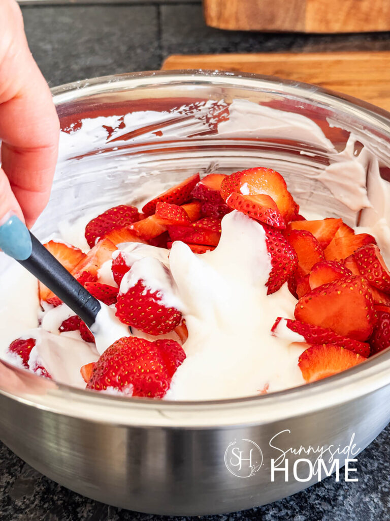 Woman folds in strawberries into the cream mixture.