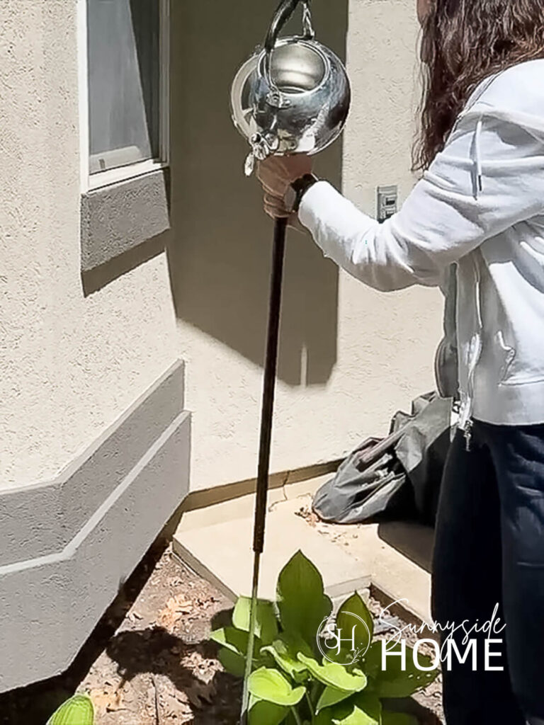 Woman place garden teapot onto the garden stake.