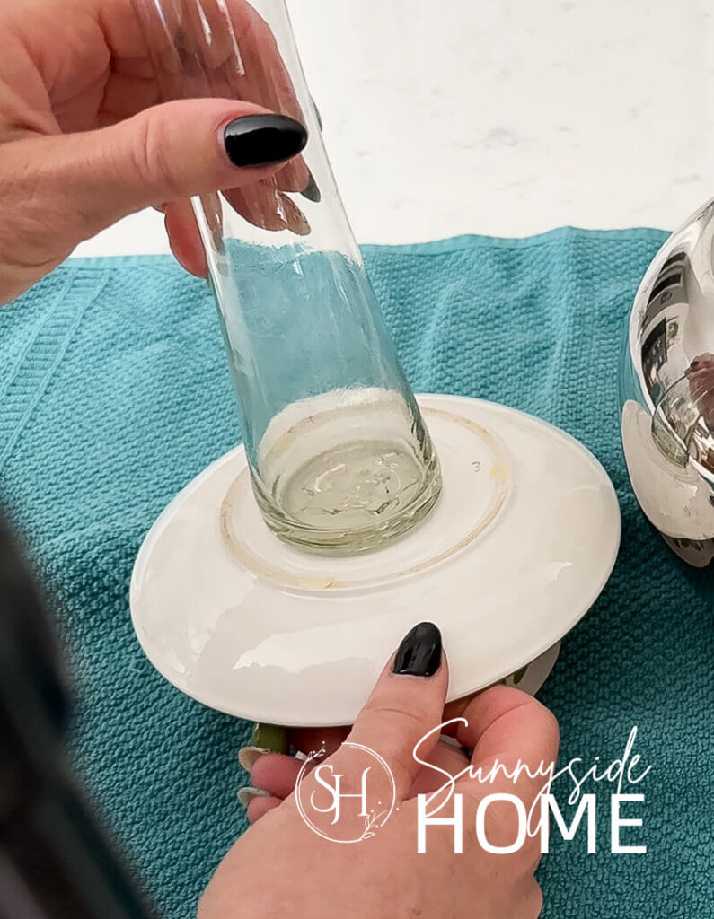 Woman attaches a bud vase to the bottom of a teacup and sauce with E6000 glue.