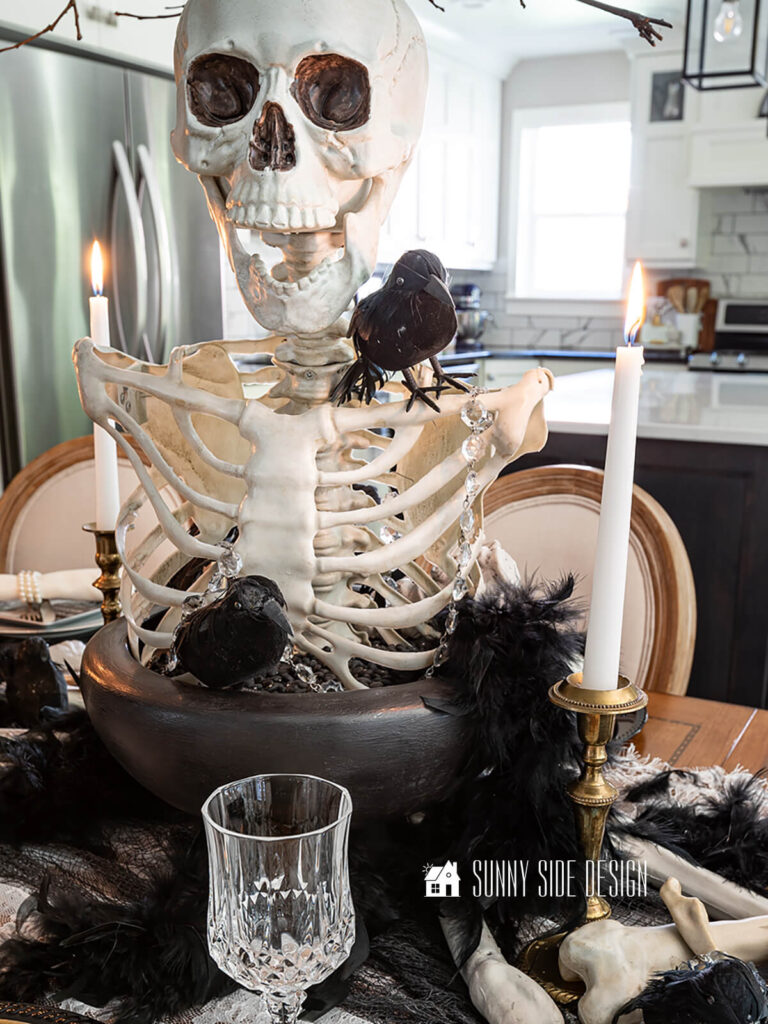 The top of a skeleton is the centerpiece for this Halloween tablescape, placed in a black container and embellished with birds, chandelier crystals and feathers.
