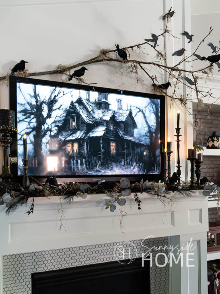 Decorating for Halloween above the mantle: a branch is hung on the wall with command hooks and embellished with spanish moss and black birds. Atop the mantle are black candles in thrifted black candlesticks and eucalyptus, twigs and birds.