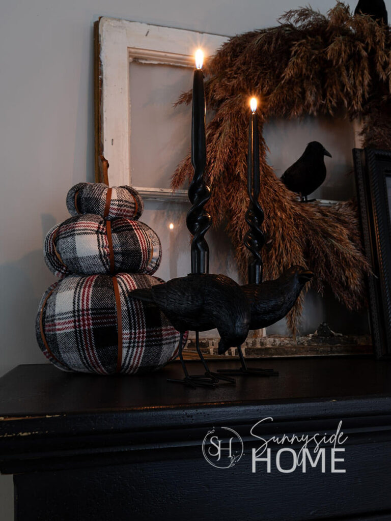 Atop the hutch is a plaid pumpkin stack, bird candlesticks and a feathery pampas grass wreath adorned with black birds.
