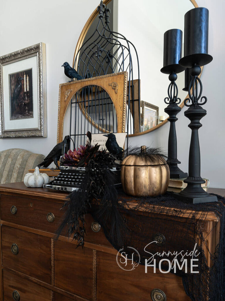 Vintage dresser decorated for Halloween with black candles on candlesticks, gold pumpkin candle, Vintage typewrite embellished with spooky flowers and birds,  and a line from "The Raven", vintage picture frame, black fence and pumpkins.