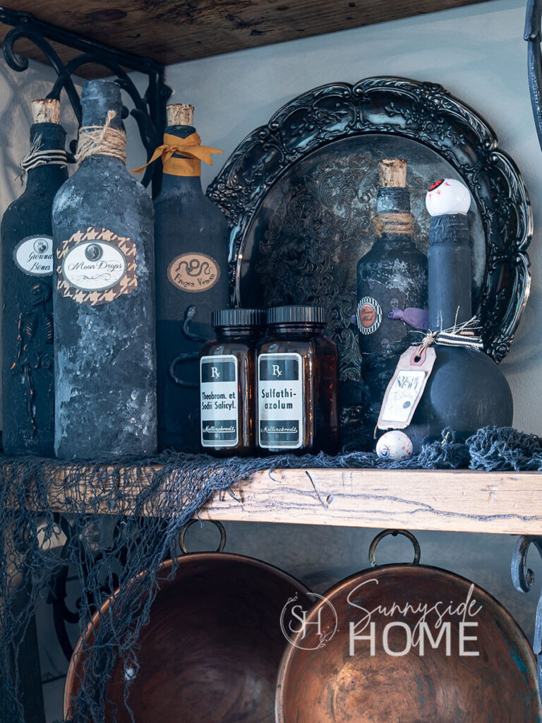 Kitchen shelves are decorated for Halloween with creepy cloth, vintage RX bottles and a mix of potion bottles on open shelves.
