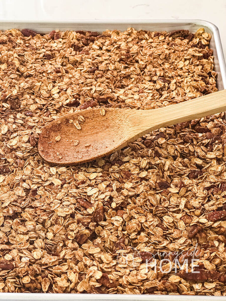 Wooden spoon used to spread homemade granola on a sheet pan.