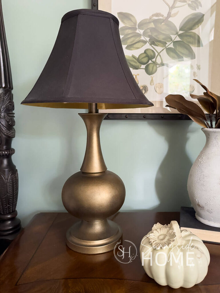 Faux antique brass finish on a thrift store lamp base with a black shade on a nightstand.