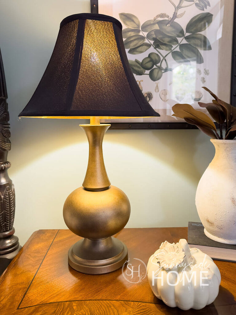 Faux antique brass finish on a thrift store lamp base with a black shade on a nightstand.