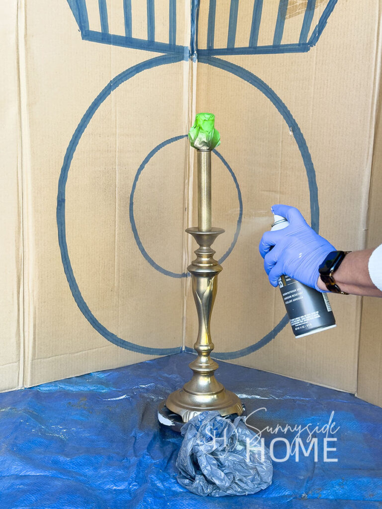 Woman applies antique brass spray paint to a shiny gold 90's lamp base.