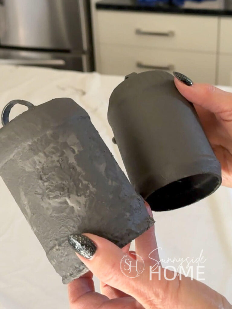 Woman holds two bells showing difference in texture with the grey undercoat of paint.