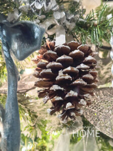 Frosted pinecone Christmas ornament hanging on a Christmas tree.