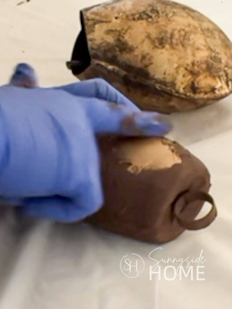 Woman applies Antique gold Rub n Buff over brown undercoat of bell made from recycled materials.
