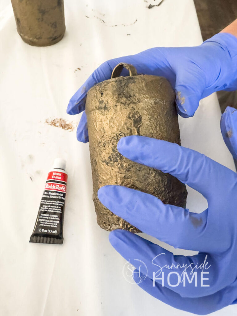 Woman gently rubs on ebony Rub 'n Buff over textured bell surface.