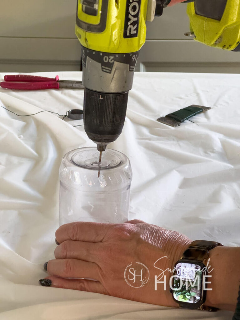 Woman drills 2 small 1/8" olds into the bottom of the recycled peanut butter jar.
