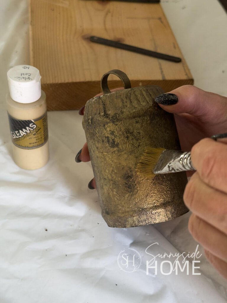 Woman applies a second coat of metallic gold craft paint to Christmas bell made from recycled materials.