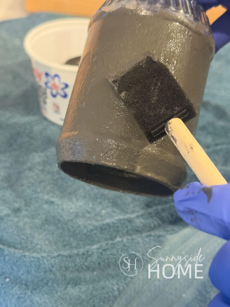 Woman uses a foam brush to pounce on textured grey paint as an undercoat for the bell project.