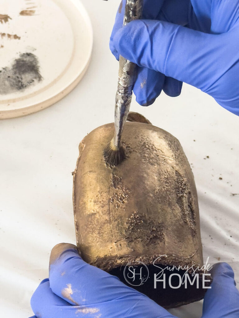 Woman lightly dabs on black Rub 'n Buff over textured areas of DIY Christmas bell.