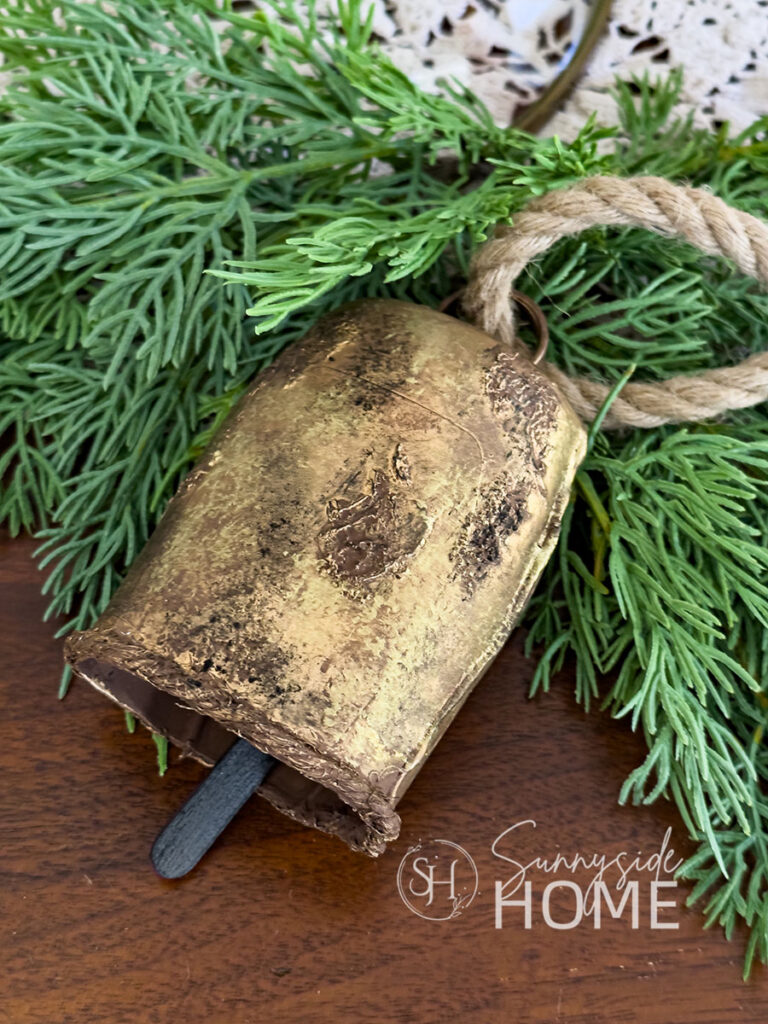 Styled DIY Christmas bell made from recycled materials with Christmas greenery on a table.