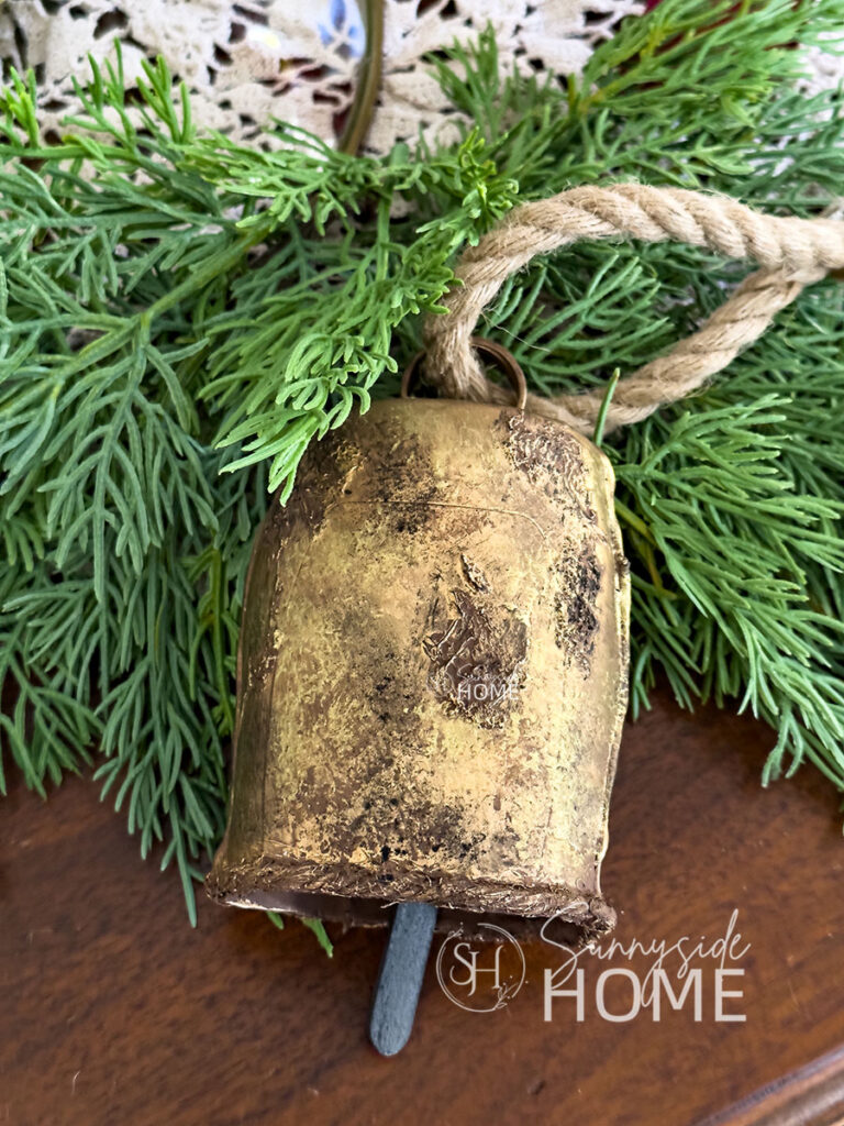 Styled DIY Christmas bell made from recycled materials with Christmas greenery on a table.