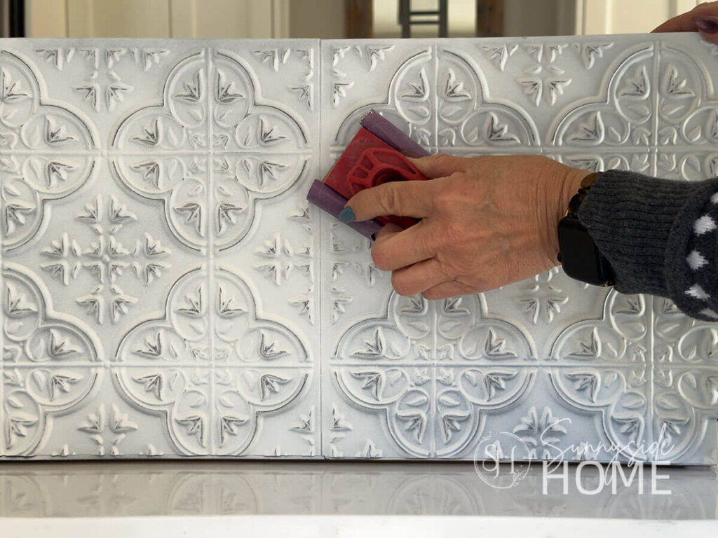 Woman distresses tiles on tree collar with fine grit sandpaper.
