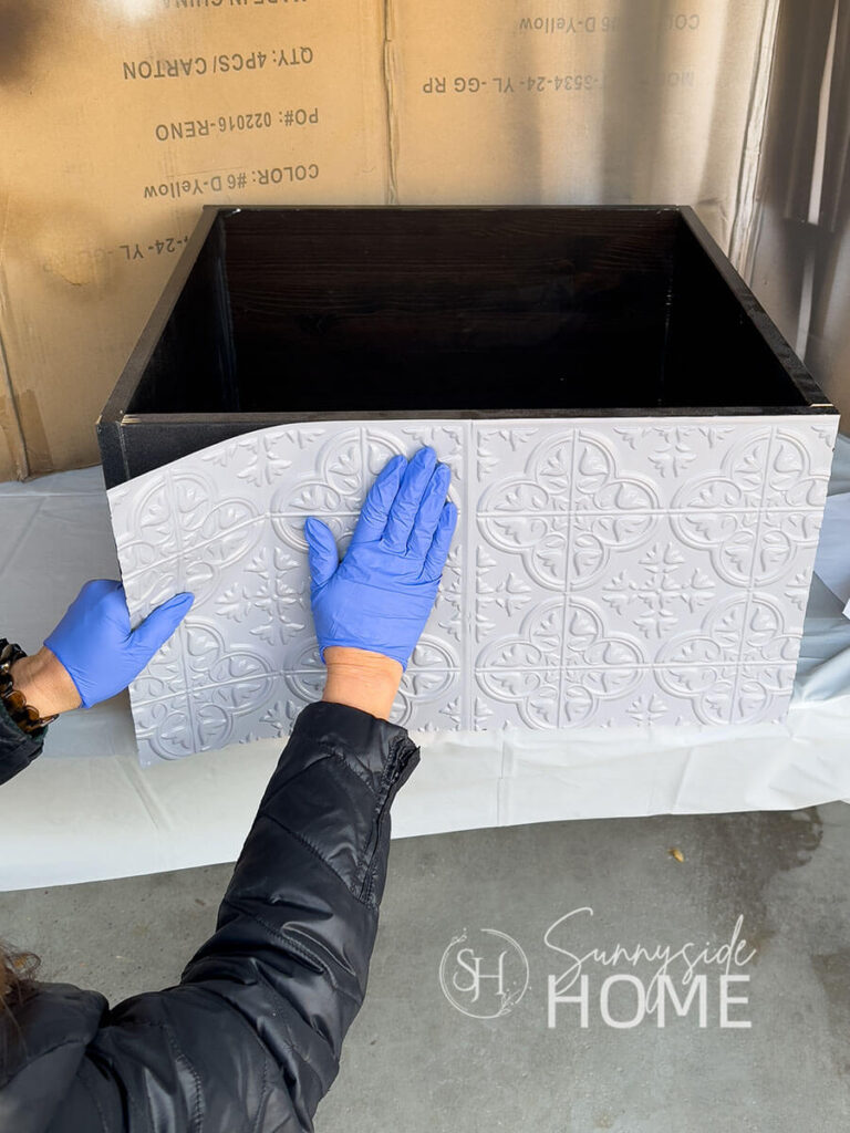 Woman presses Dollar Tree tiles to a wooden box.
