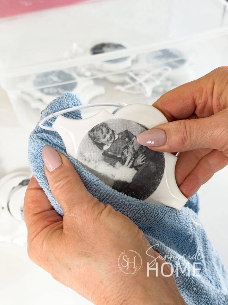 Woman dusts a Christmas ornaments with a blue microfiber cloth before placing in a storage container.