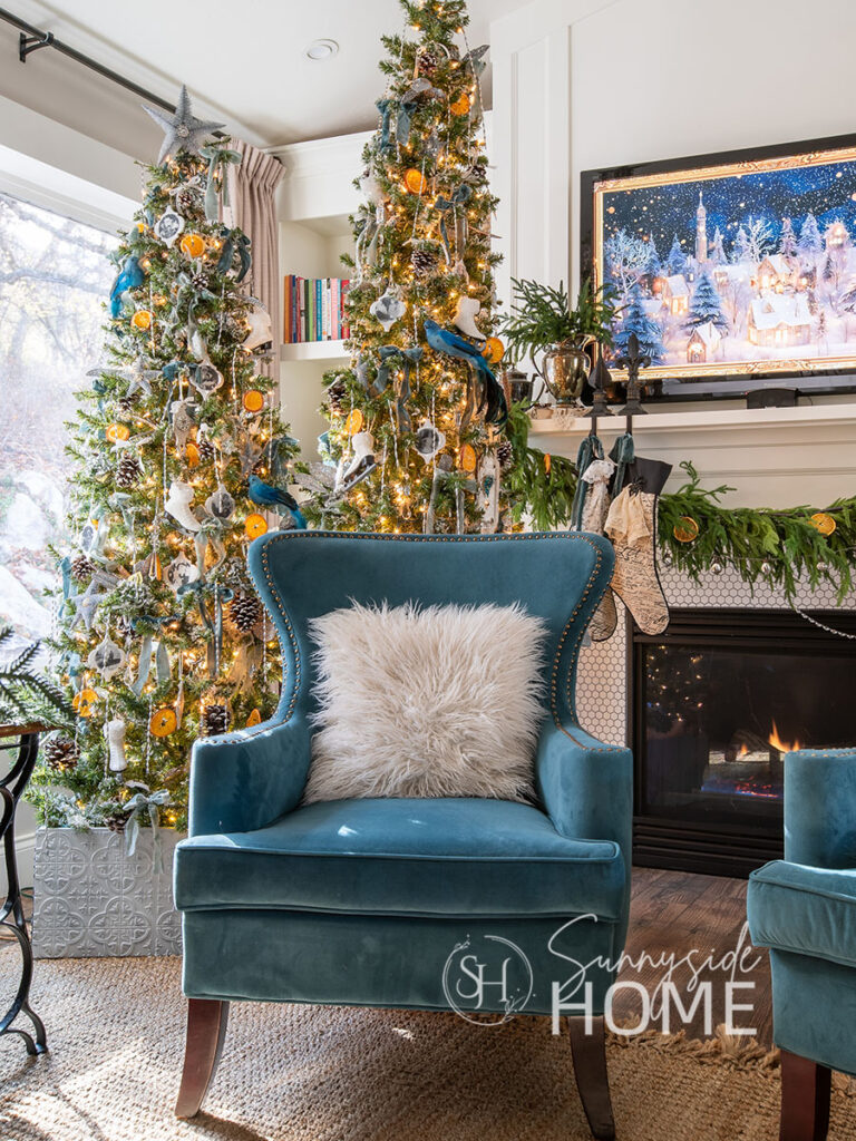 Two slim trees decorated for Christmas with a Victorian theme, personalized family photo ornaments, dried orange slices, blue velvet bows, ice skates, frosted pinecones, and Victorian tinsel.
