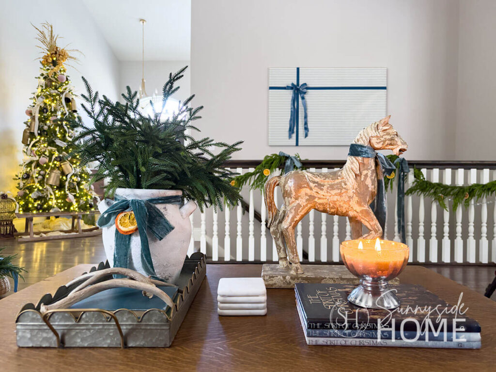 Decorate the Christmas the coffee table with an old jug vase filled with pine stems, embellished with velvet ribbon and a dried orange slice. Also on the coffee table are antlers, a mercury glass candle and a horse statue is embellished with a blue velvet bow.