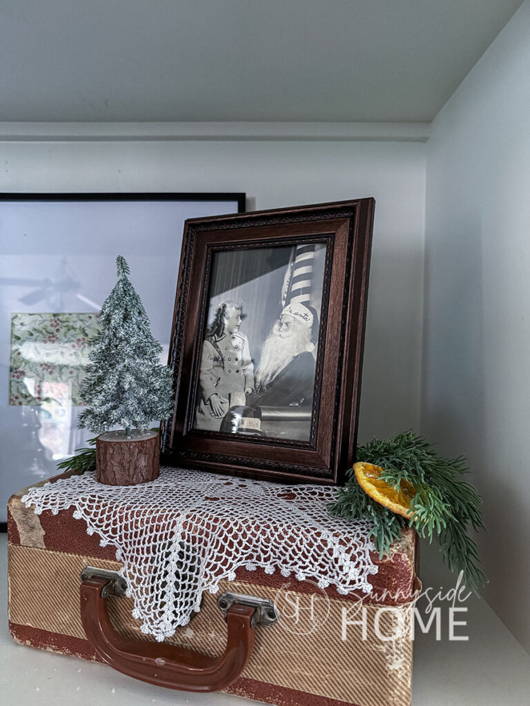 Vintage picture of little girl sitting on Santa's lap on a vintage case with a mini tree, greenery and a dried orange slice.