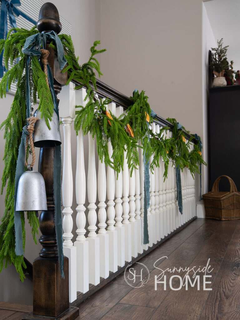 Lifelike Norfolk pine garland is draped over the railing and embellished with chandelier crystals, dried orange slices and blue velvet ribbon bows.