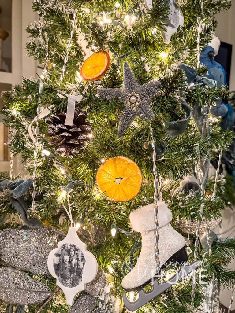 Christmas tree in the family room decorated with DIY Victorian tinsel, dried orange slices, DIY personalized ornaments, sisal tree star ornaments, blue velvet bows and frosted pinecone ornaments.