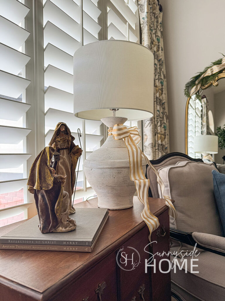Nativity on stacked books and a lamp is embellished with a gold and ivory bow.