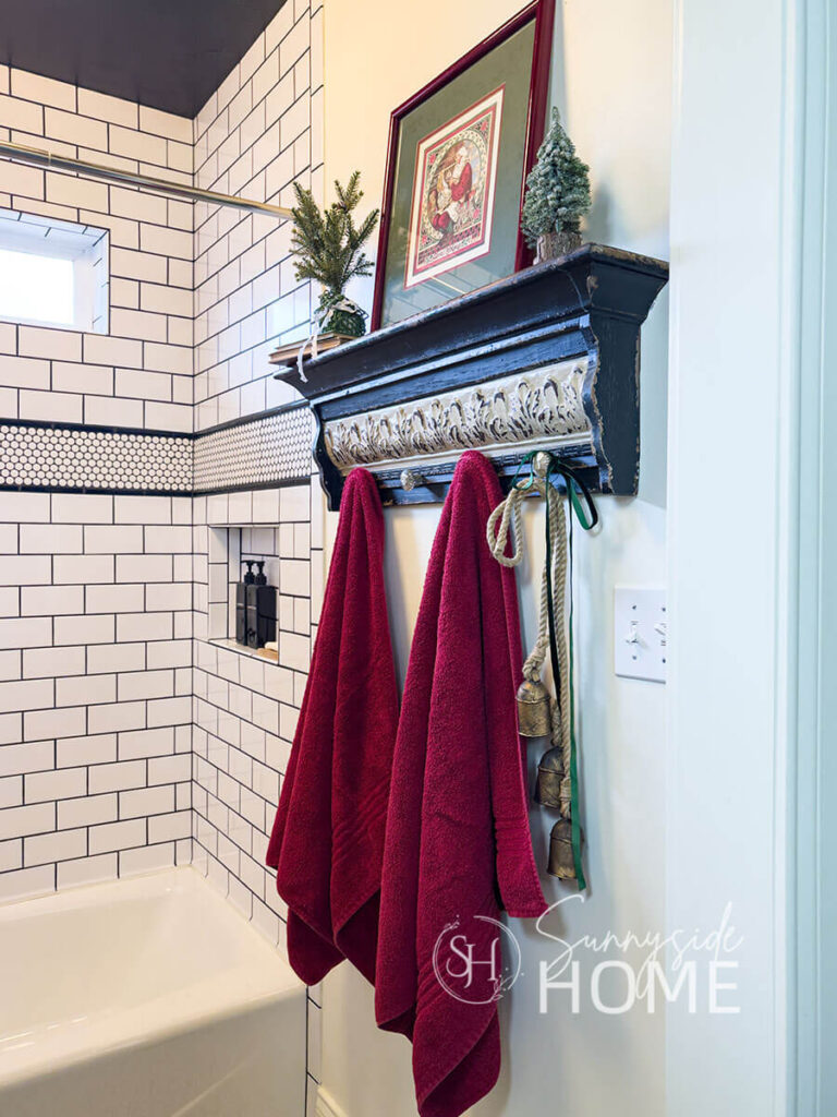 In the bathroom, red towels are hung on a black shelf and decorated with DIY faux brass bells, ribbon, mini trees and art.